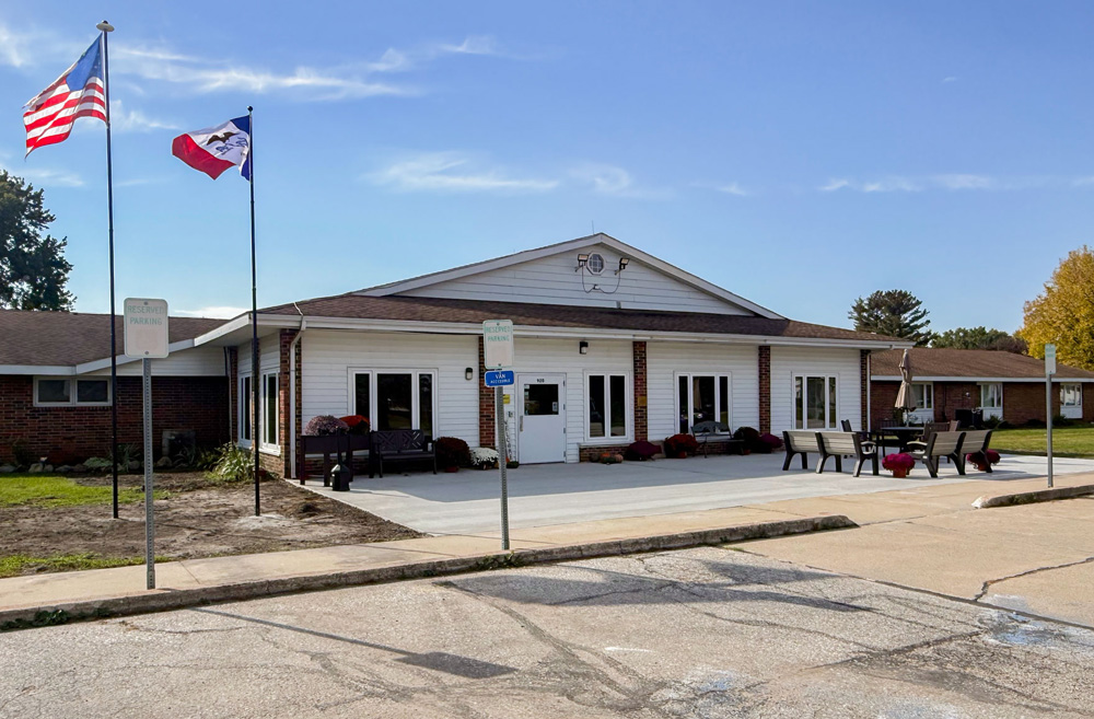 Front exterior of Shell Rock Senior Living in Iowa, featuring the updated entrance patio, outdoor seating, and flagpoles.